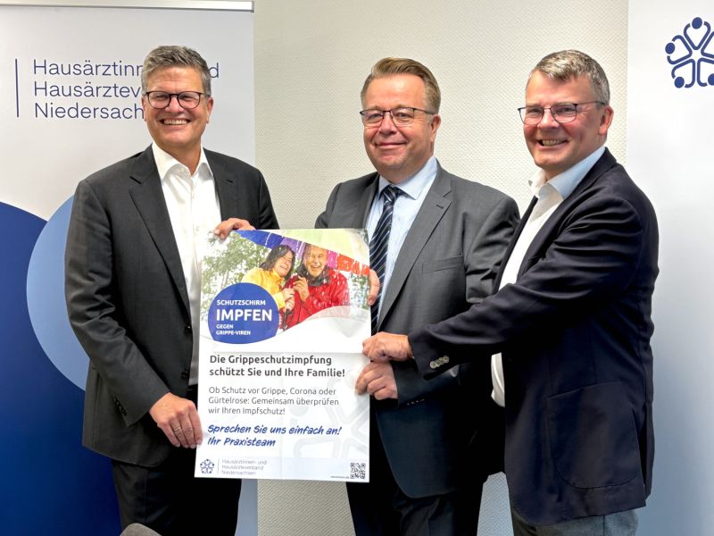 Mark Barjenbruch, Dr. Eckart Lummert sowie Dr. Matthias Berndt stehen gemeinsam vor einem Roll-up und halten ein Wartezimmerplakat zur Grippeschutzimpfung hoch.